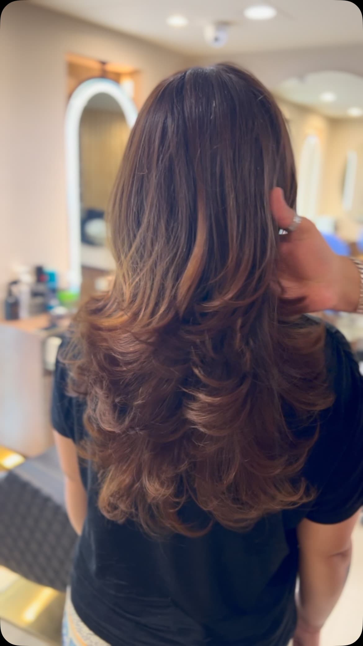 A finished layered haircut with caramel highlights, photographed from behind on the salon floor